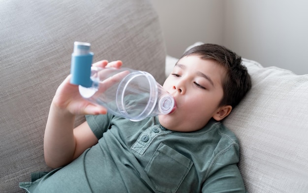 Sick child using asthma inhaler for allergiesPoor boy tired from chest coughing holding inhaler spacerTried Kid having asthma allergy