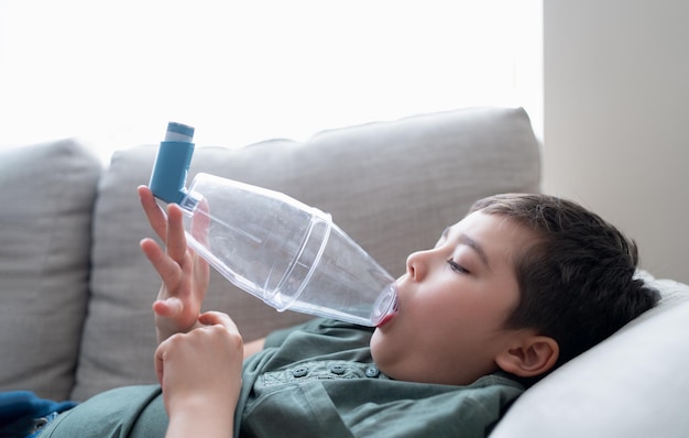 Sick child using asthma inhaler for allergiesPoor boy tired from chest coughing holding inhaler spacerTried Kid having asthma allergy