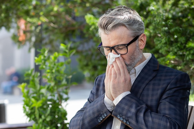 Sick and cold mature adult man sitting on bench outside office building businessman in business suit