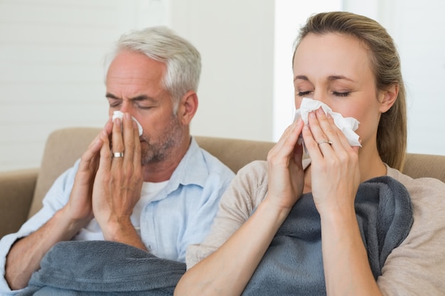 Sick couple blowing their noses sitting on the couch