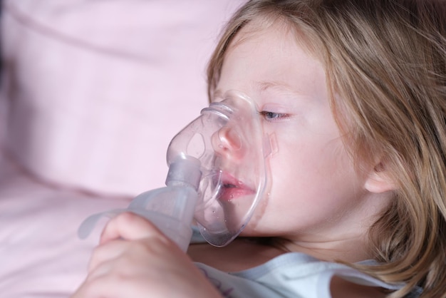 Sick girl in oxygen mask lies on hospital bed