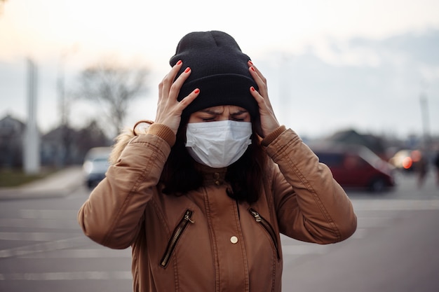 Sick ill girl wears medical mask anxious woman in mask suffering from heat, headache struggles on the street, feeling bad. Person needs help. Virus, Chinese pandemic coronavirus, panic concept.