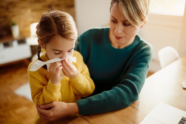 Sick little girl blowing nose in a tissue at home