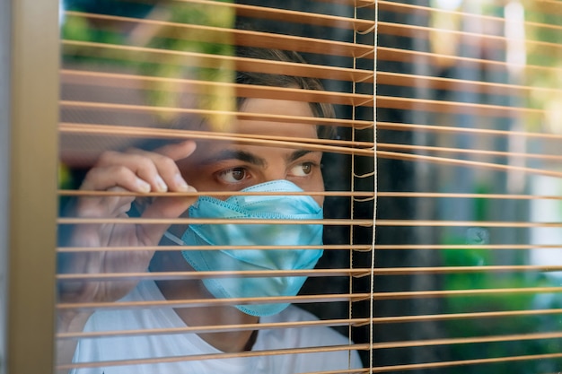 Sick man of corona virus looking through the window and wearing mask protection and recovery from the illness in home. Quarantine.