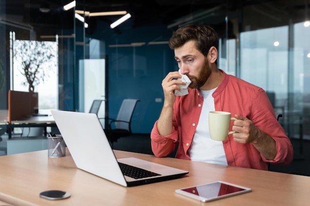 Sick man at work has flu and cold businessman sneezes and coughs at workplace working inside office