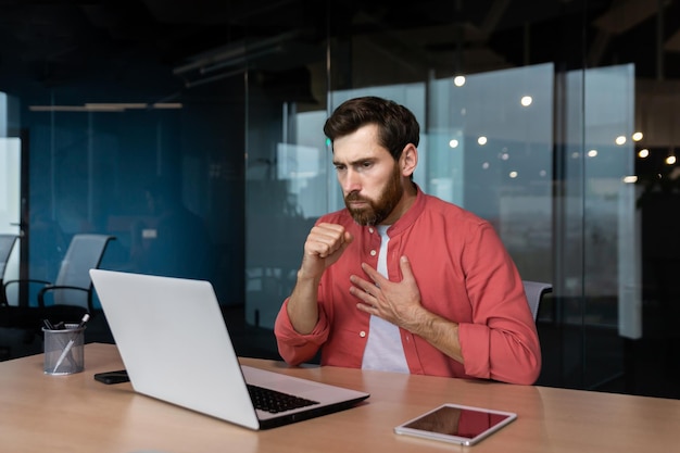 Sick man at workplace mature worker in red shirt coughing businessman inside office at work using