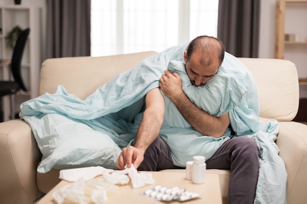 Sick man wrapped in blanket reaching out for knapkins during self isolation.