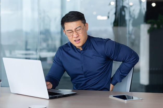 Sick overworked man at work businessman has severe back pain asian man holding hand on side