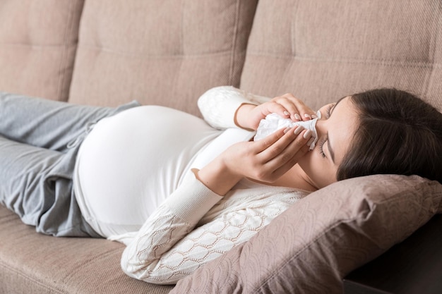 Sick pregnant woman blowing nose into tissue at home Healthy millennial healthcare concept