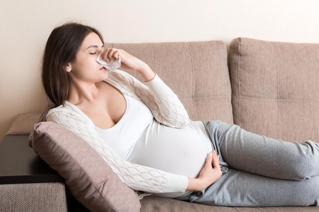 Sick pregnant woman blowing nose into tissue at home Healthy millennial healthcare concept