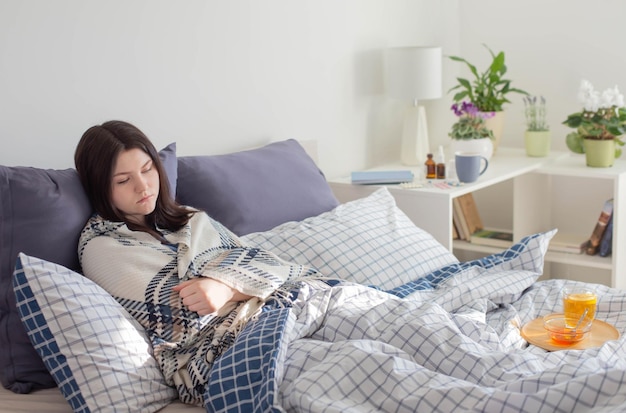 Sick teen girl with tea on bed in white room