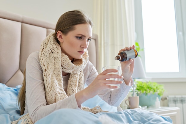 Sick woman at home in bed adding drops of medicine to a glass of water