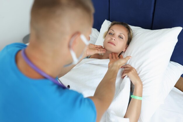 A sick woman lies in bed the doctor checks the lymph nodes closeup home emergency call