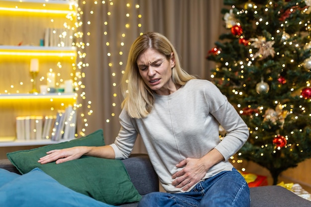 A sick woman sits at home alone has a severe stomach ache at christmas near the christmas tree on