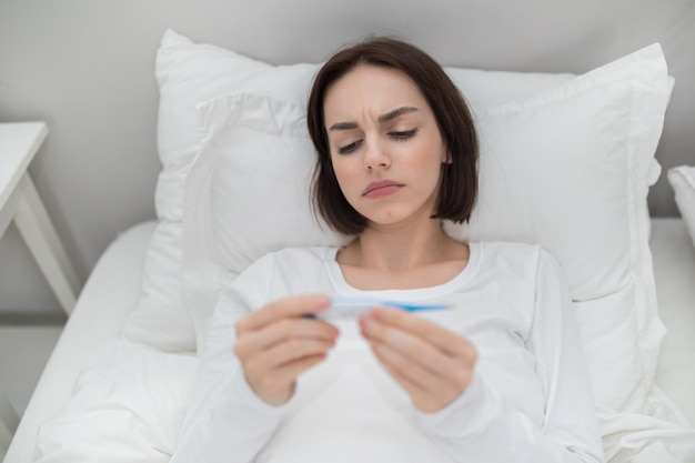 Sick woman with fever checking her temperature resting in bed