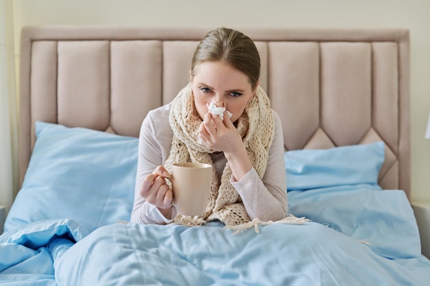 Sick young woman in bed with handkerchief and cup