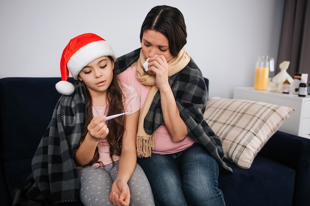 Sick young woman hold white tissue close to nose and look at thermomenter