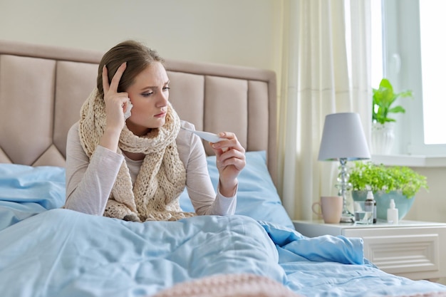 Sick young woman with in hands sitting at home on bed