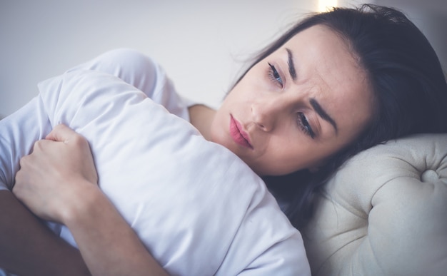 Sickness. Close-up photo of a sick girl, who is lying in her bed and hugging a pillow.