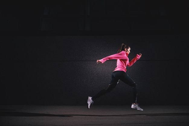 Side motion view of sexy fit athlete running girl in sportswear at the street in front of the grey wall.