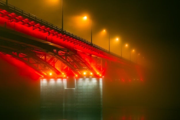 Side night view of the illuminated bridge in foggy weather Bridge in the fog