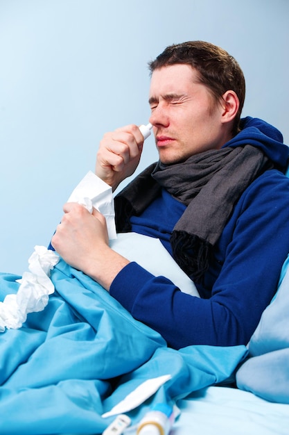 Side photo of sick brunet male using nasal spray while lying in bed