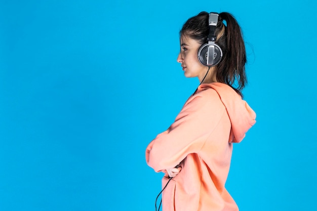 Side photo of young beautiful girls standing on blue background and listening music High quality photo