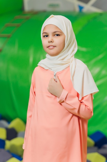 Side portrait of a little Muslim girl wearing a hijab. Concept of Muslim clothing for children. against the background of the playground.