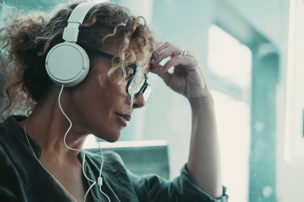 Photo side portrait of a woman with headphones listening music or podcast alone thoughtful female people at work indoor leisure activity at home attractive lady touch her front worried people problems