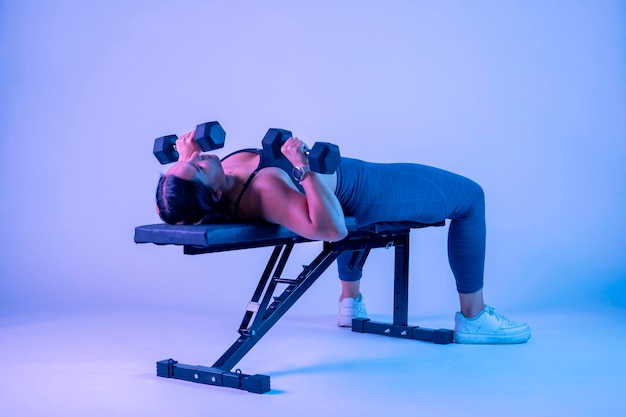 Side shot of a woman bench pressing with two dumbbells