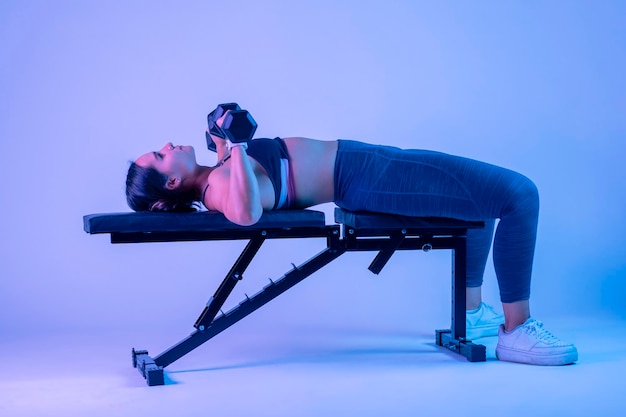 Side shot of a woman bench pressing with two dumbbells