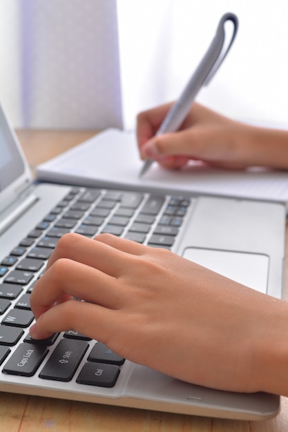 Side view of accountants hands doing paperwork on cork desktop and laptop keyboard