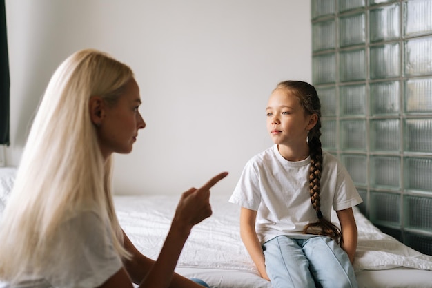 Side view of angry young mother scolding raising voice scream and gesturing with hands at stubborn difficult little child daughter at home