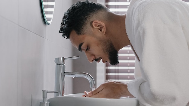 Side view arab spaniard indian arab man guy opens faucet near washbasin at home in hotel bathroom