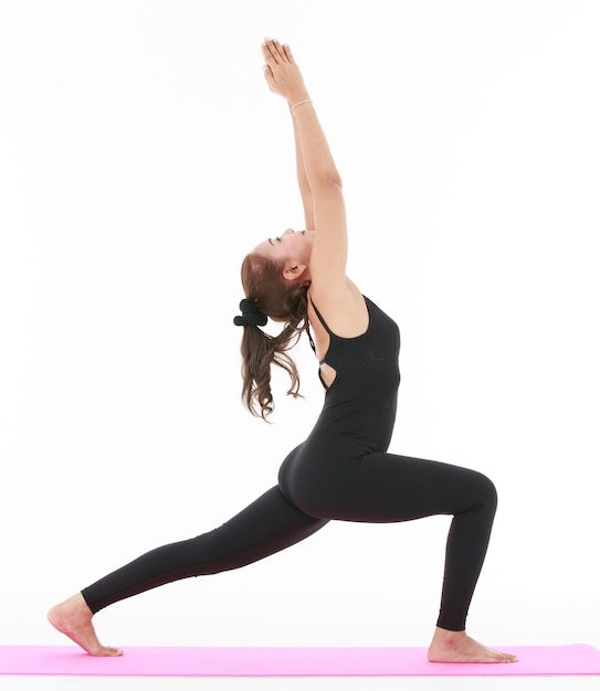 Side view of Asian female doing Crescent Lunge pose with raised arms while practicing yoga against .