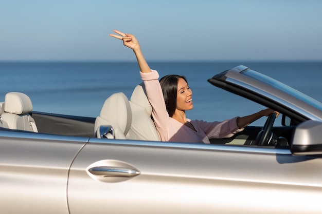 Side view of asian girl riding cabriolet and holding hand up on sunny day