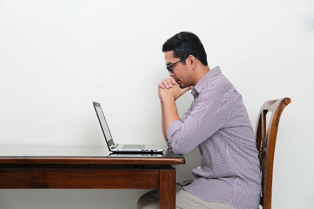 Side view of Asian man looking to his laptop with serious focus expression