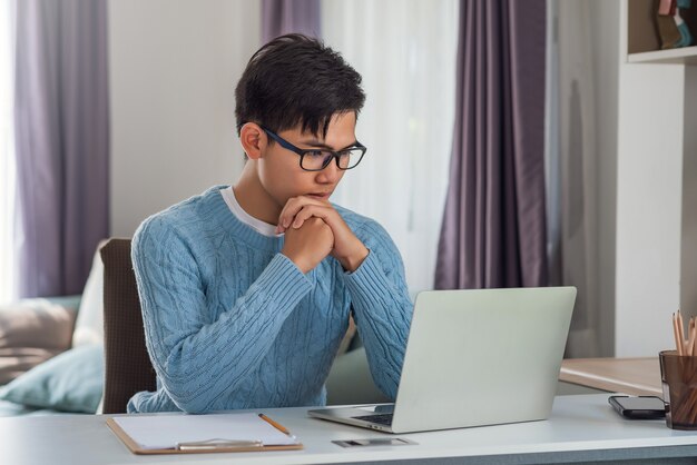 Side view of an Asian man working at a home desk using a tablet.