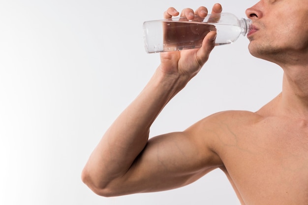 Side view of athletic man drinking water from bottle with copy space