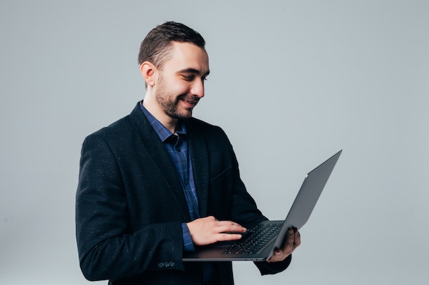 Side view of attractive young businessman in classical suit using laptop, standing against gray background