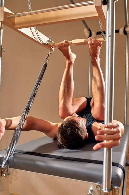 Side view of barefoot male athlete lying on pilates reformer and performing abs exercise during fitness workout Pilates man concept