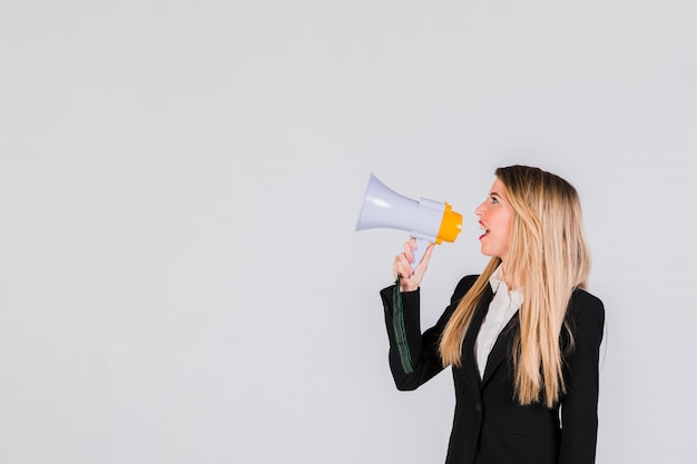 Side view of blonde young woman shouting through megaphone against grey backdrop