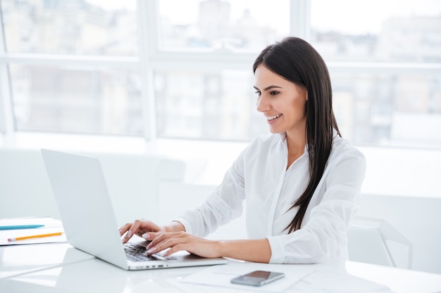 Side view of business woman using laptop and sitting by the table in office