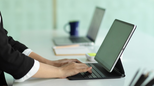 Side view of businesswoman hands typing on tablet keyboard on white table in office room