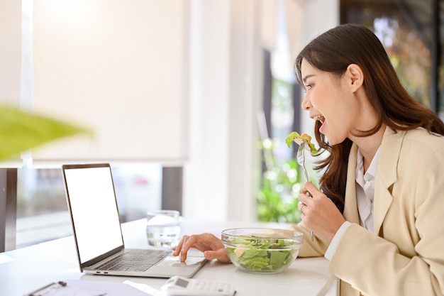 Side view of a busy and hungry asian businesswoman having lunch at her desk while working