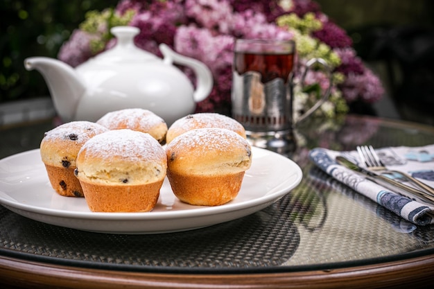 Side view of cakes on white plate and white teapot and a glass of tea with purple flowers background