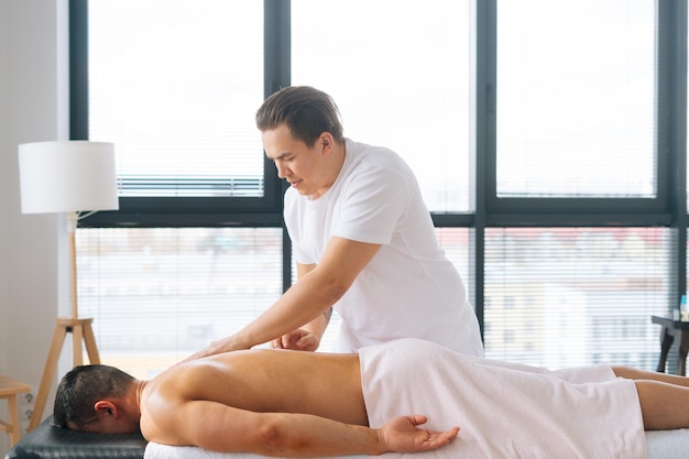 Side view of caucasian male masseur massaging back of muscular sportsman lying on massage table on