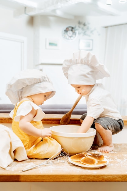 Side view of a charming caucasian cooks boy and girl making dough for pancakes