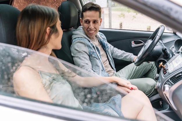 Side view of cheerful couple smiling inside a car seat. Horizontal portrait of caucasian man traveling by car on a rainy day. People and travel concept.