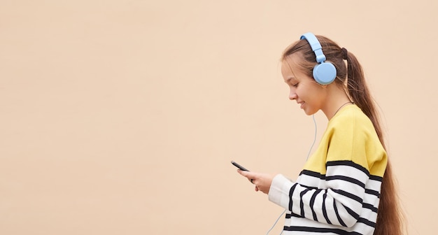 Side view of a cheerful teenage girl using blue headphones listening to music on a colored background